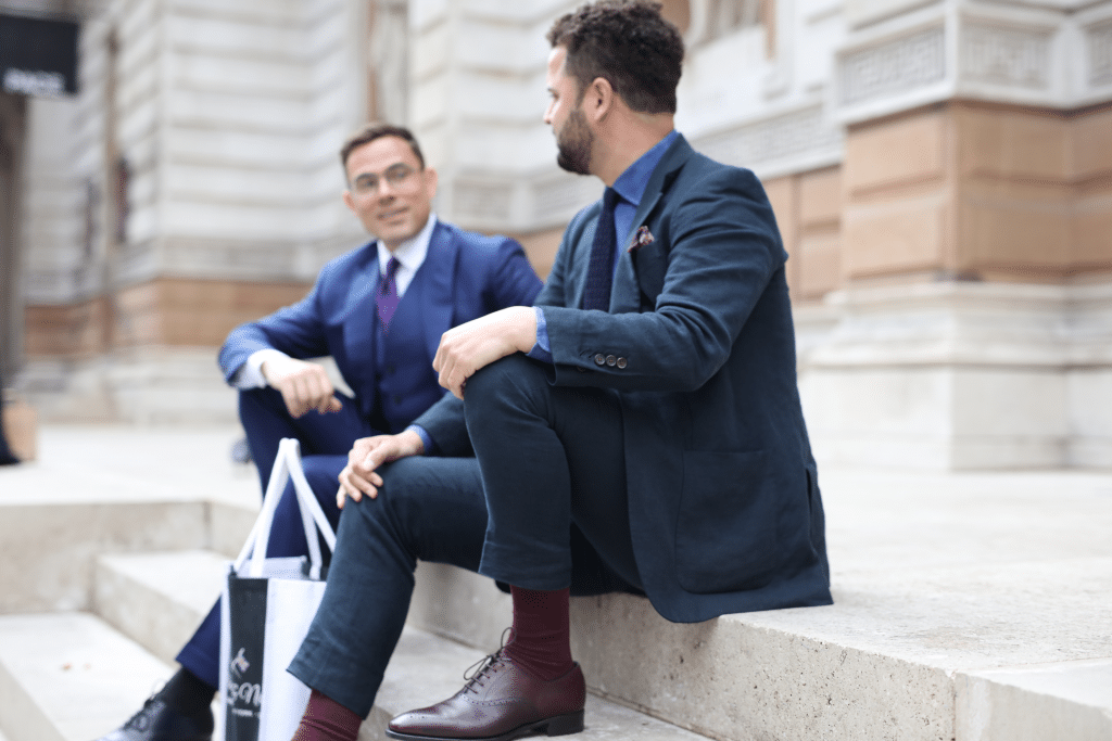 Ian Fielding-Calcutt and partner, founders of Fielding & Nicholson, in a candid moment on steps outside, reflecting bespoke tailoring elegance.