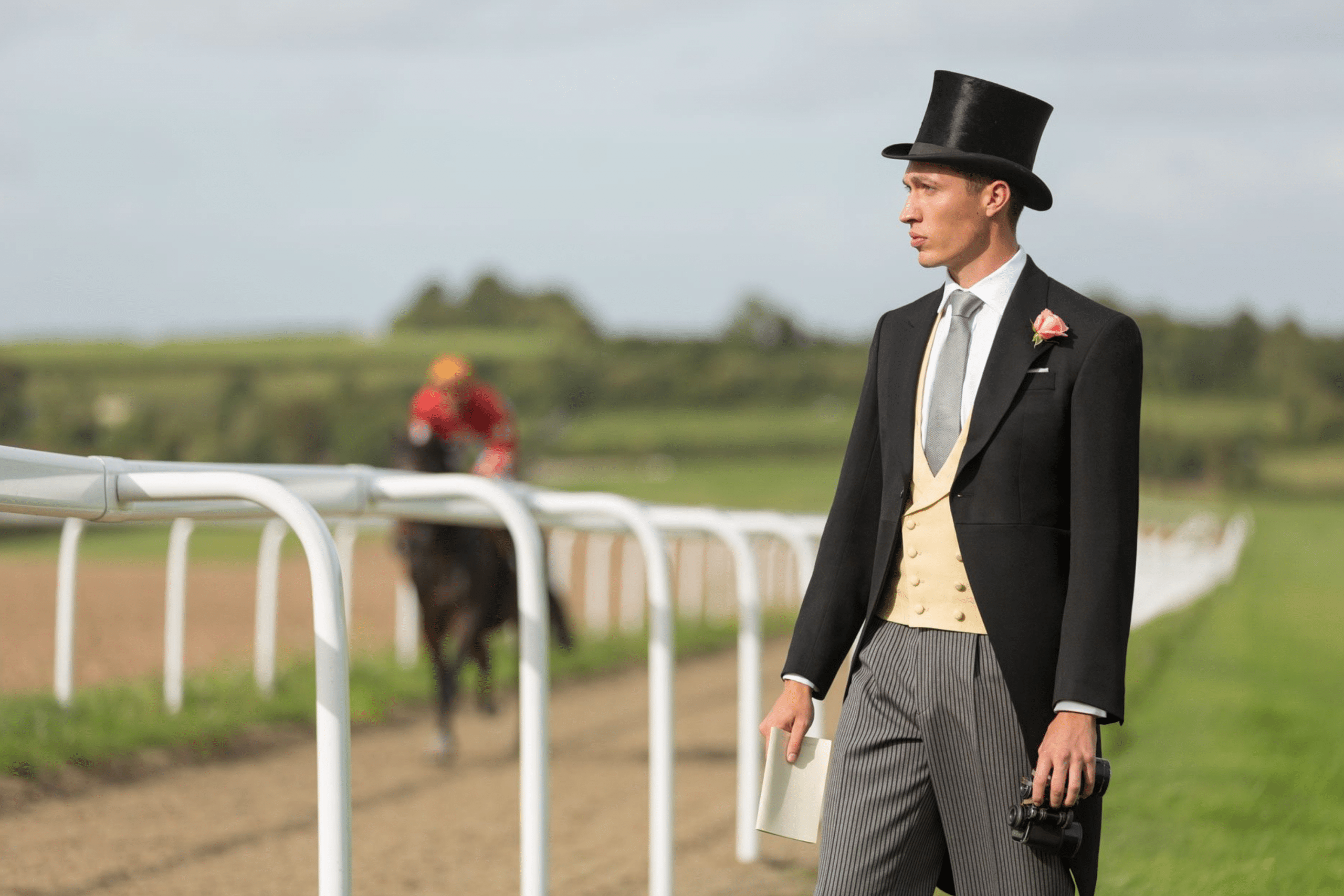 A dapper gentleman epitomizing the Guide to Race Day Attire, stands poised at the racetrack in a bespoke morning suit with a top hat, symbolizing sartorial race day elegance.