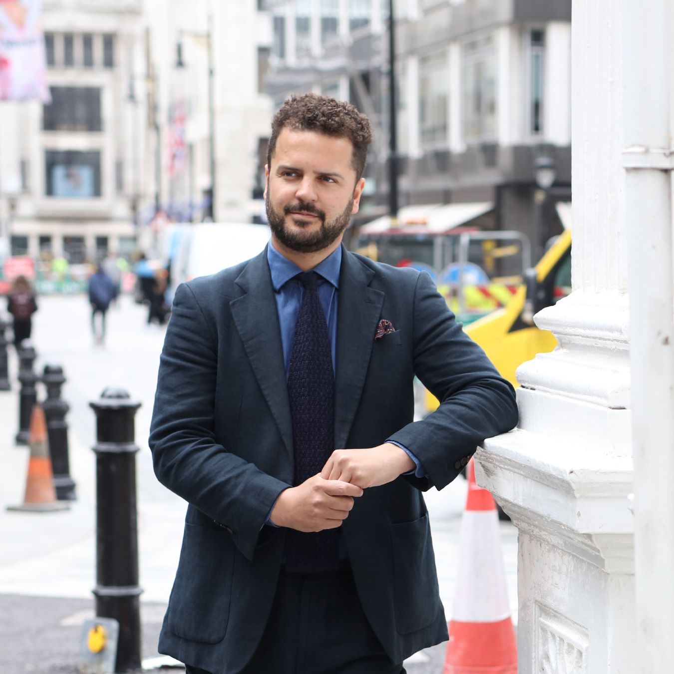 Man wearing a tailored single-breasted navy suit with a crisp blue shirt and silk tie, ideal for business settings.