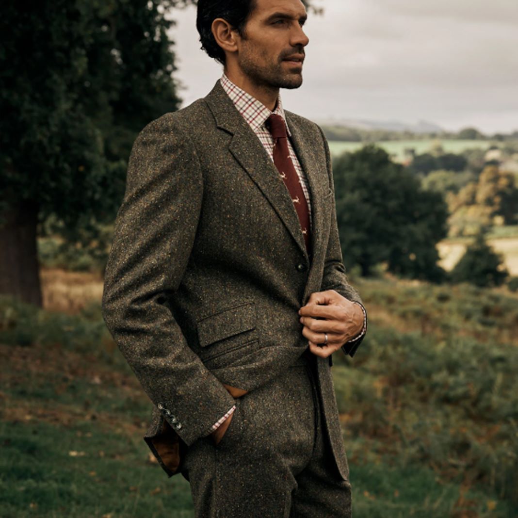 Man adjusting the buttons on his tweed suit, styled with a wool scarf for a country event.