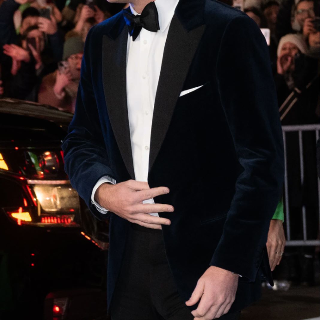 Man adjusting the buttons of a  velvet dinner suit styled with patent leather shoes and a black bow tie.