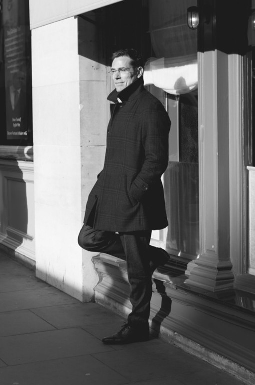 Monochrome photo of man in a dark coat and suit, walking with confidence.