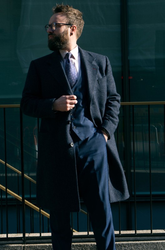 Man in a navy wool overcoat and suit, exuding classic business style.