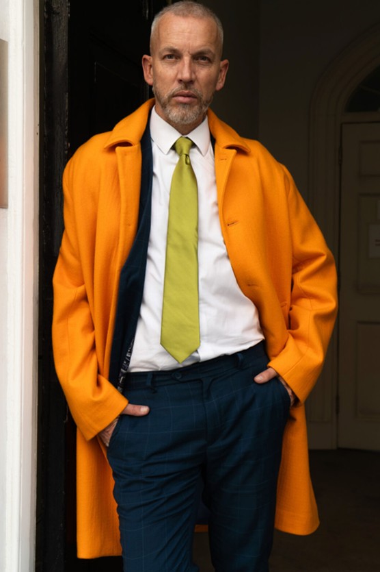 Bold orange overcoat worn with a white shirt and yellow tie – striking winter outfit.