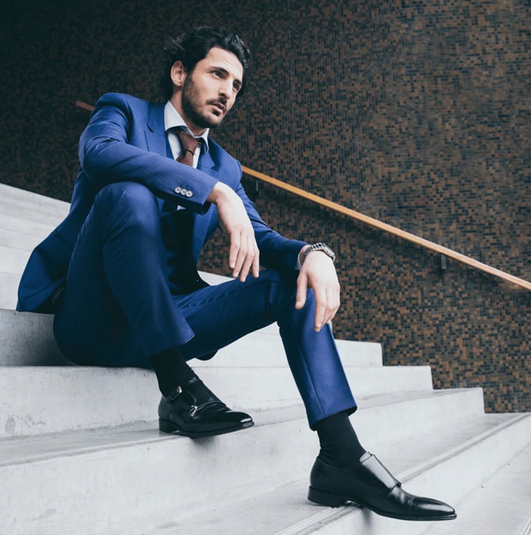 A photo of a man sitting on steps wearing a bespoke suit and polished shoes