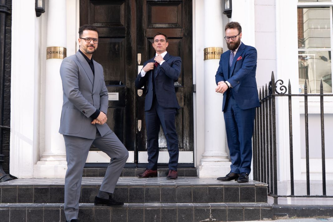 a photo of a team of luxury tailors standing at the steps of their showroom in london