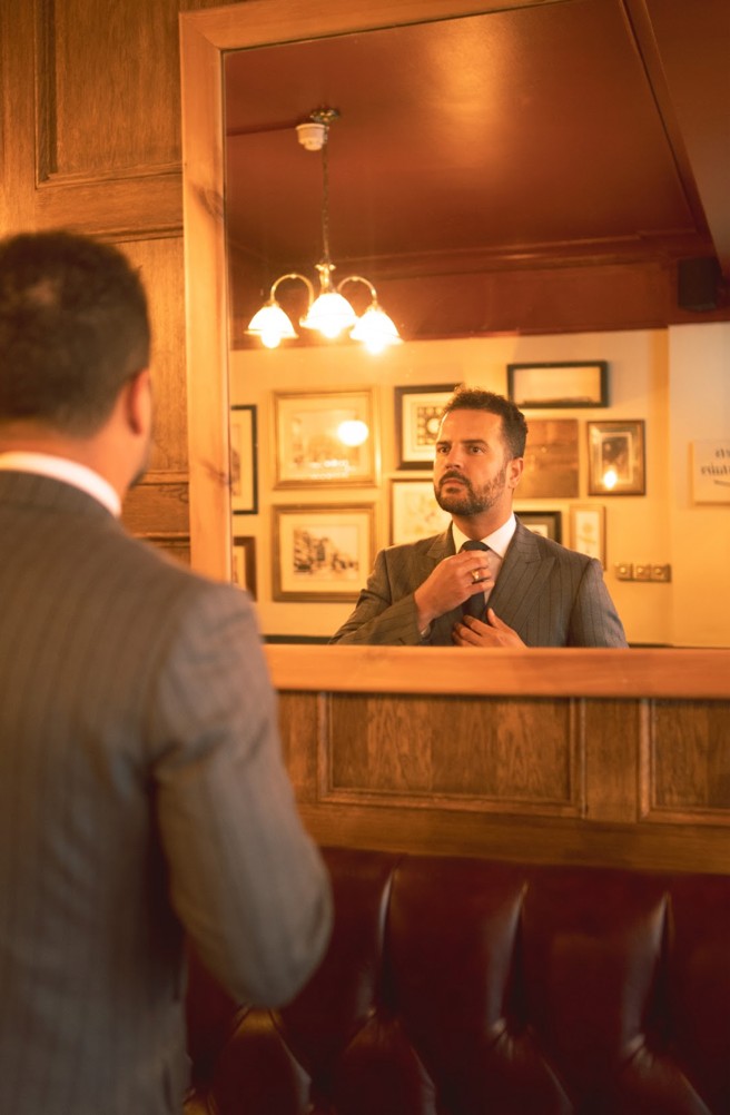 A man in a tailored suit adjusting his appearance in a stylish London barbershop, capturing refined grooming and menswear.