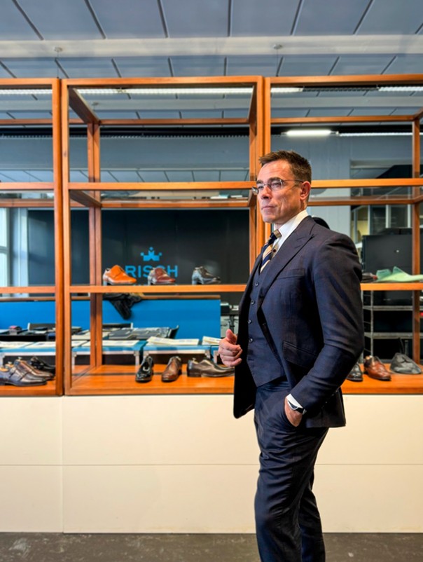 A man in a navy suit standing in a contemporary London environment, showcasing polished businesswear.