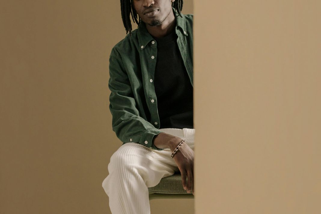 a photo of a man wearing a green shirt over a black t shirt and white trousers