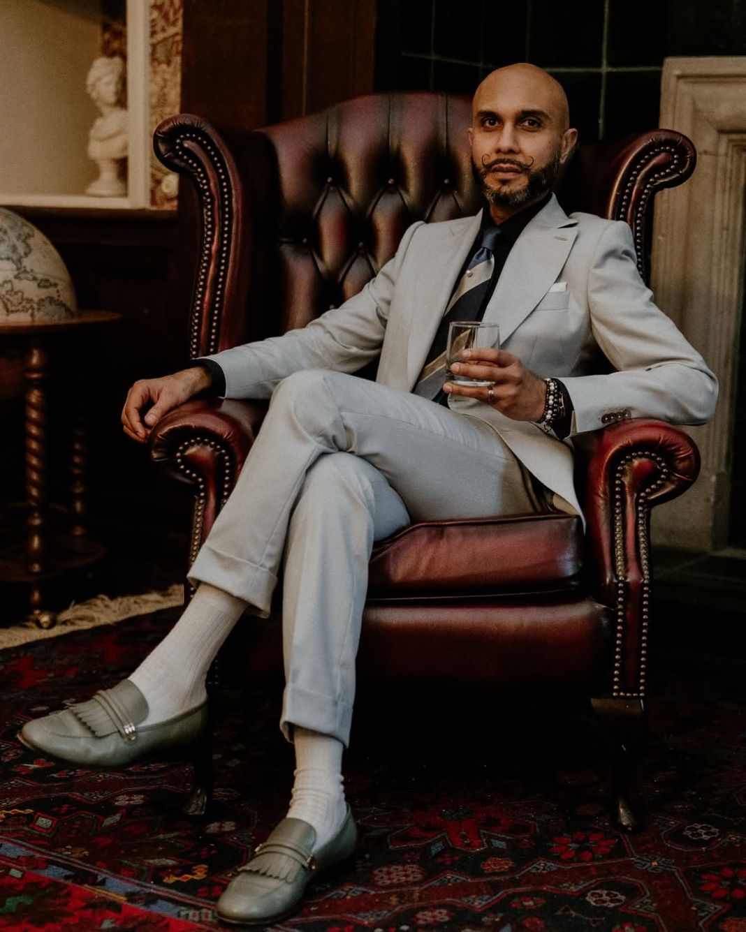 a gentleman in a custom suit enjoying a drink on a comfy chair