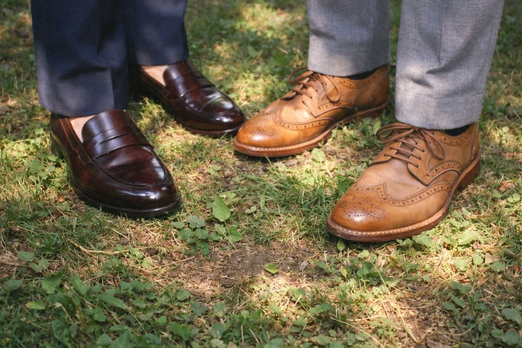 An illustrative image of polished brown loafers and tan brogues standing on uneven grass