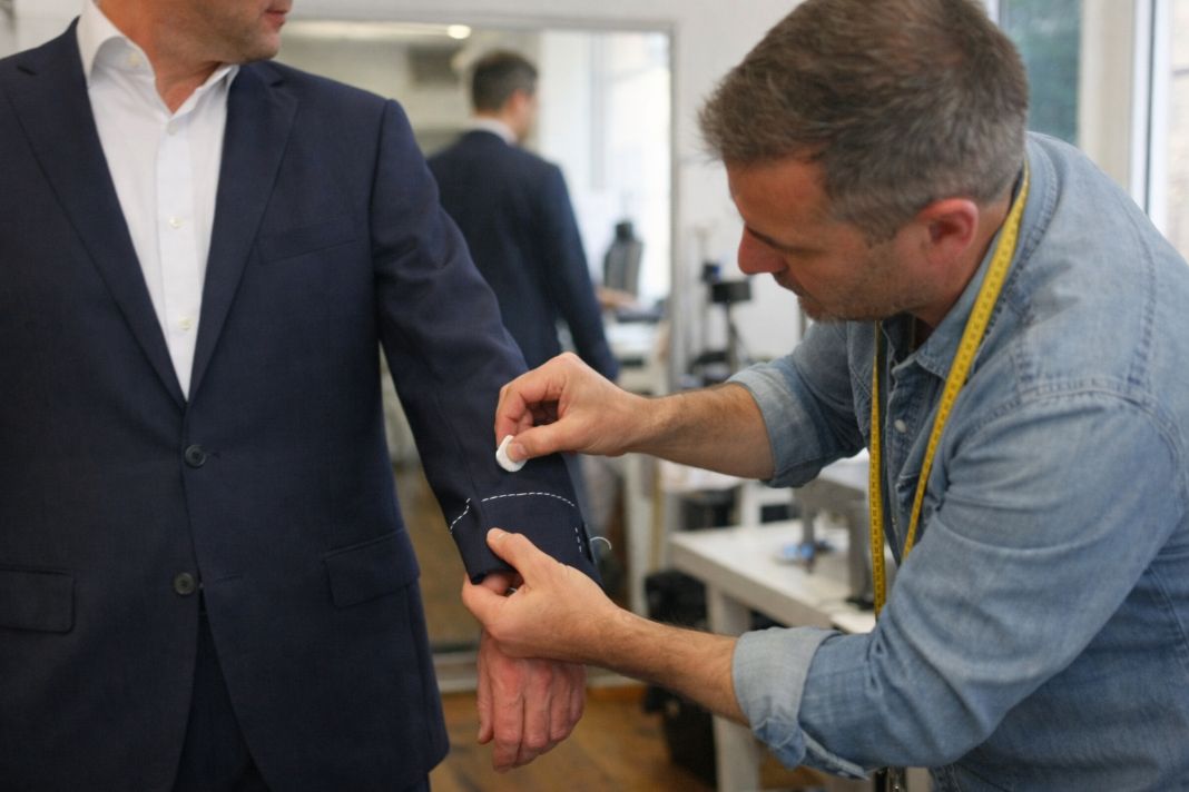 an illustrative photo of a tailor marking sleeve adjustments on a client’s jacket during a personalised fitting session