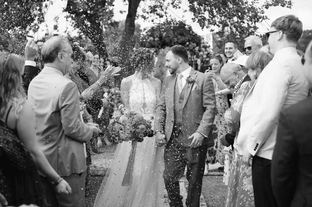 Bride and groom outdoors with guests, in autumn wedding attire