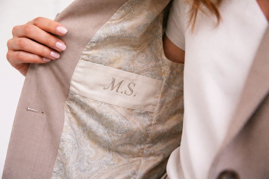 An illustrative photo of a close-up interior of a womans suit jacket showing a subtle monogram and patterned lining