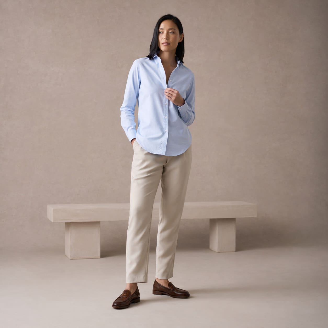 Woman in a light blue button up shirt with beige straight leg trousers, sample image