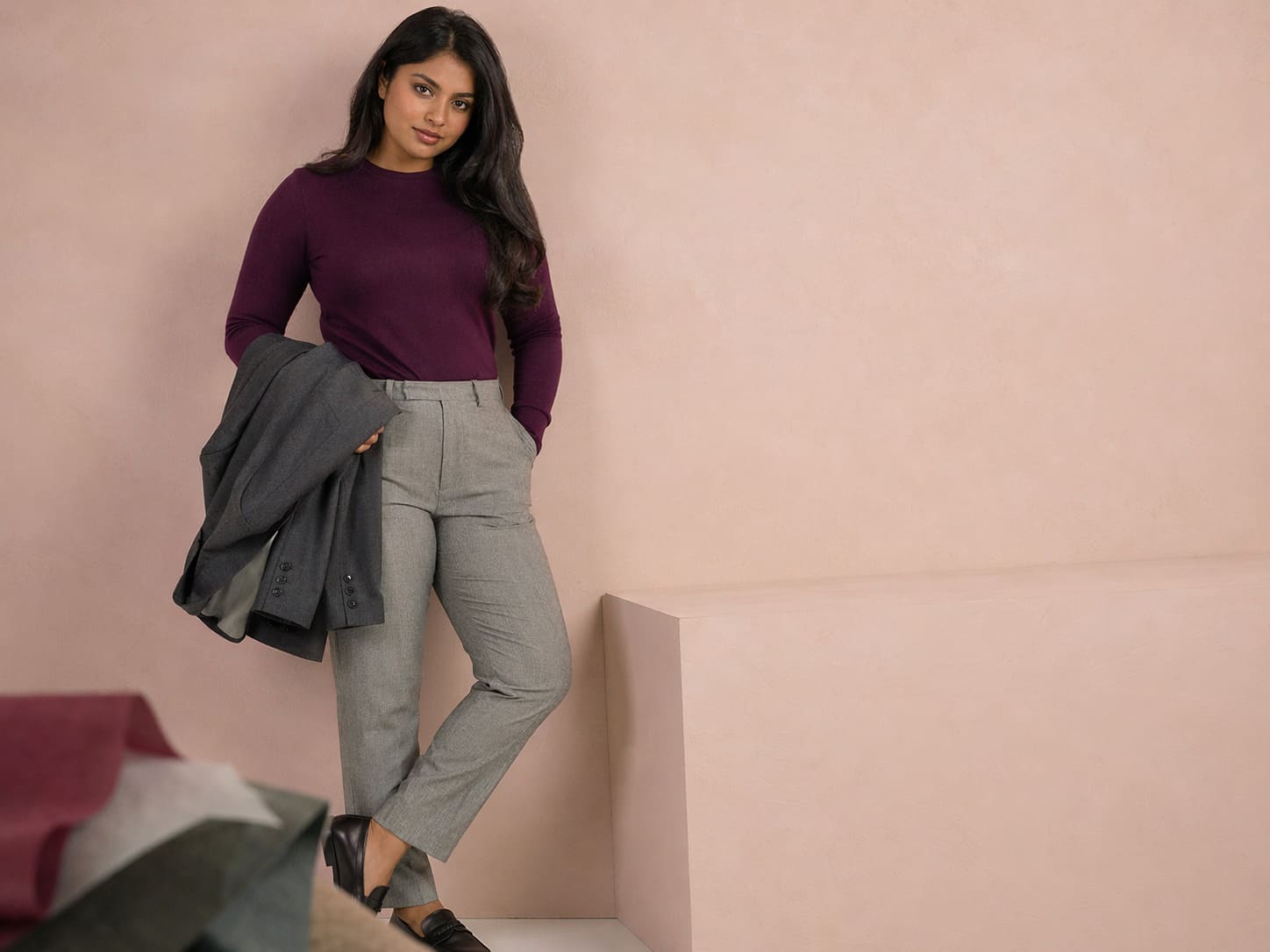 Woman in a plum knit top with grey slim fit trousers, sample image