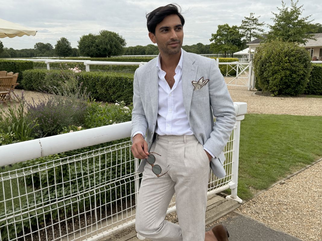 An illustrative image of a light grey summer blazer, white open-collar shirt, stone tailored trousers, brown suede loafers