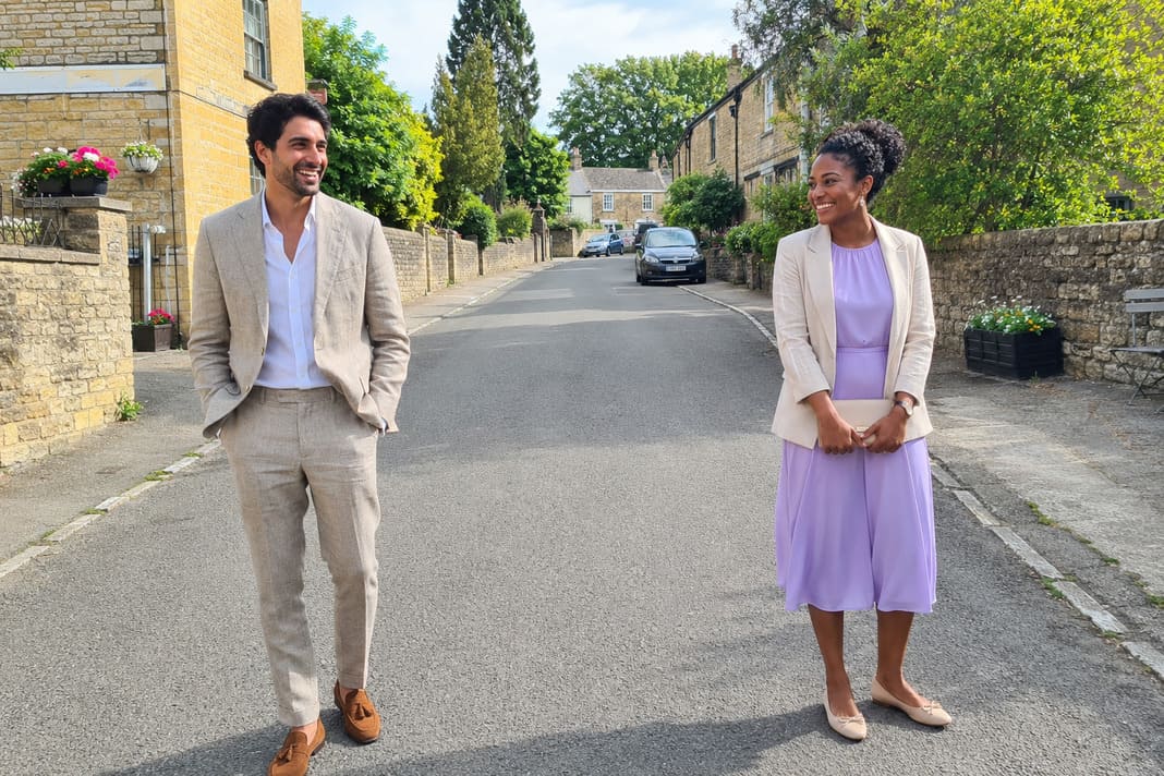 A man wears a light beige linen suit with an open-collar white shirt while a woman pairs a lilac midi dress with a coordinating tailored blazer, creating elegant and breathable summer christening outfits for warm-weather celebrations. A man wears a light beige linen suit with an open-collar white shirt while a woman pairs a lilac midi dress with a coordinating tailored blazer, creating elegant and breathable summer christening outfits for warm-weather celebrations.
