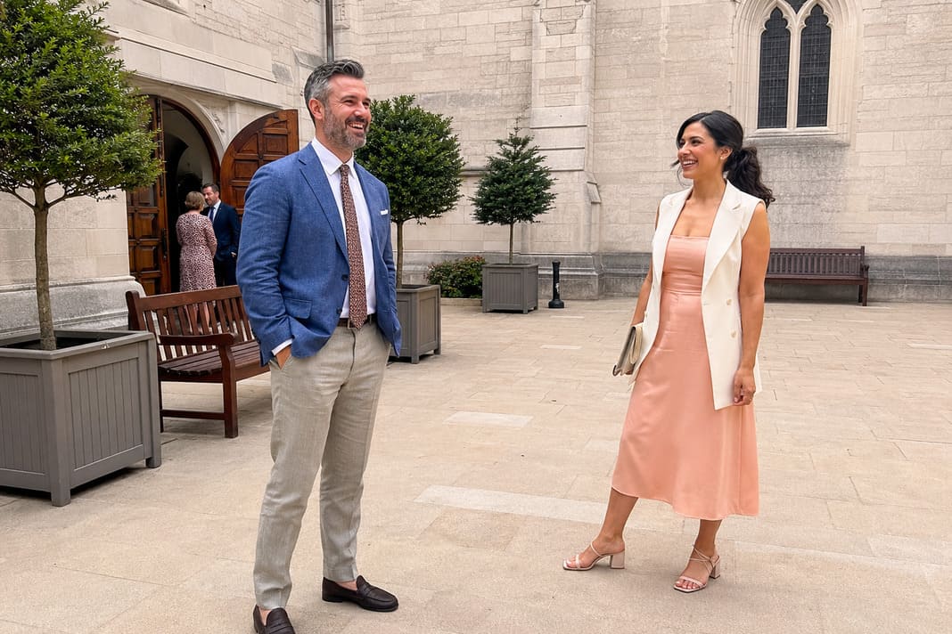 A blue tailored suit with a crisp white shirt is paired with a peach sleeveless midi dress, demonstrating sophisticated summer christening outfits that balance formal style with breathable warm-weather fabrics.