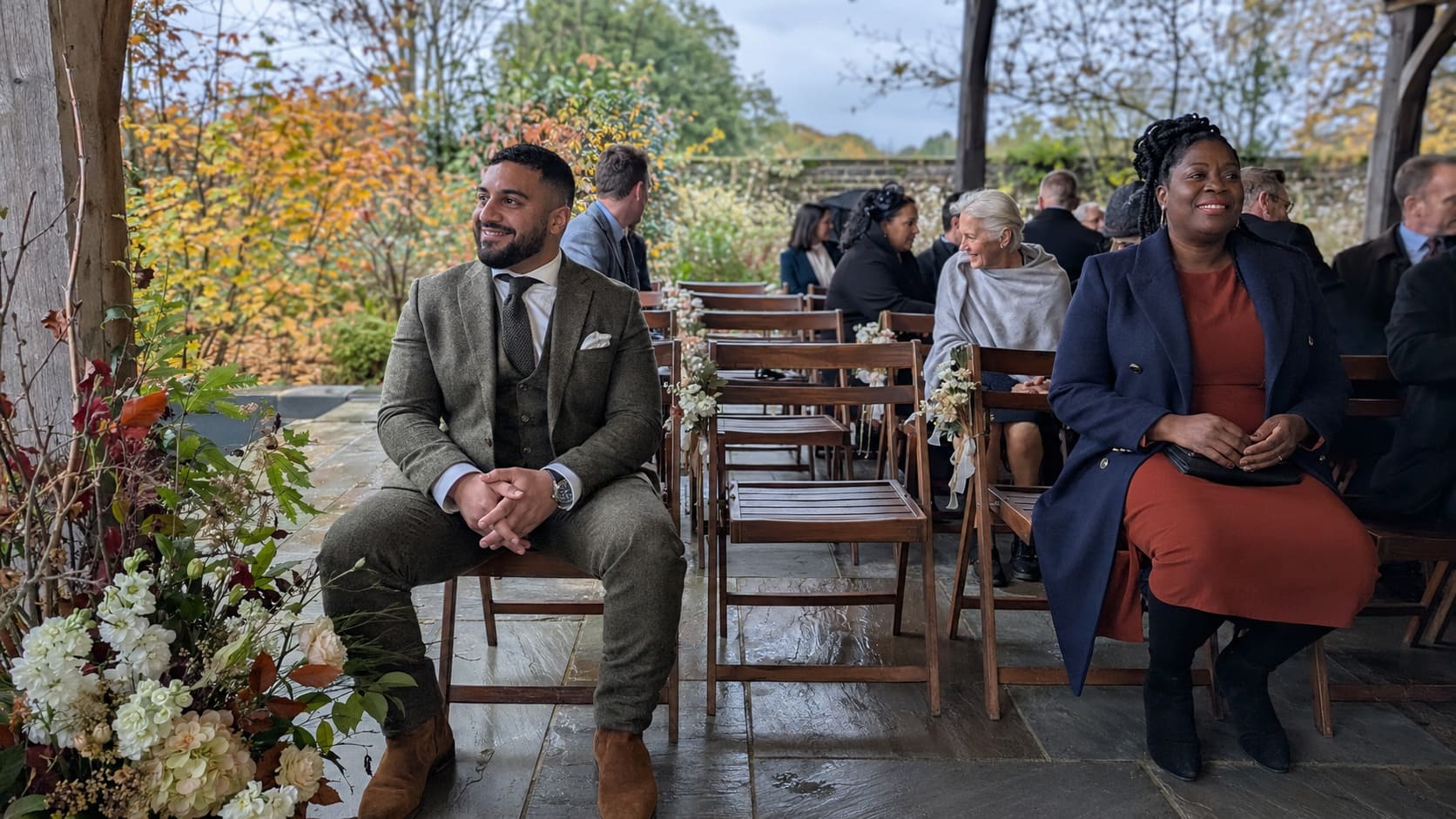 Guests wearing layered autumn tailoring sit outdoors together during a relaxed seasonal social event.