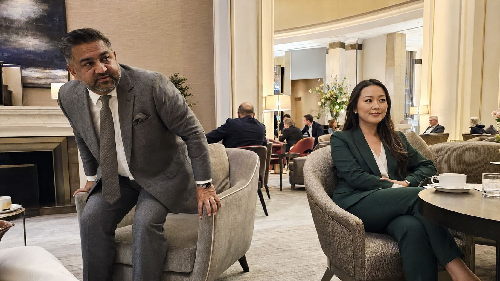 Man wearing grey suit and woman wearing green tailoring relax in bespoke clothing together indoors. Man wearing grey suit and woman wearing green tailoring relax in bespoke clothing together indoors.