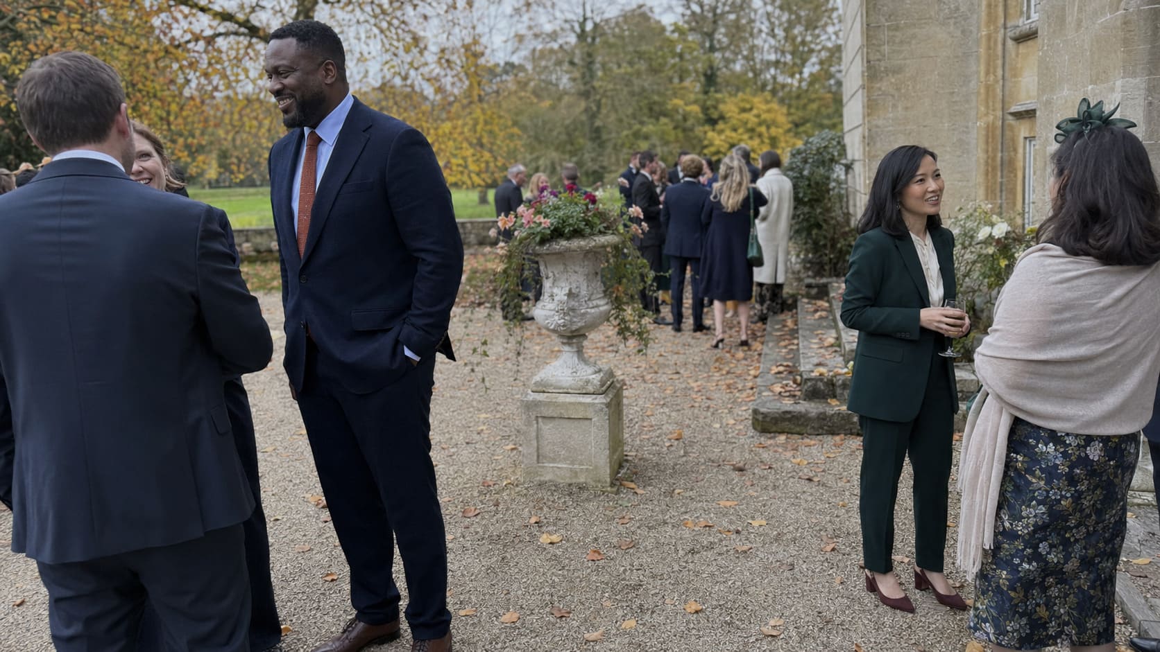 Men wearing navy suits talk at an outdoor autumn reception beside casually dressed guests. Men wearing navy suits talk at an outdoor autumn reception beside casually dressed guests.