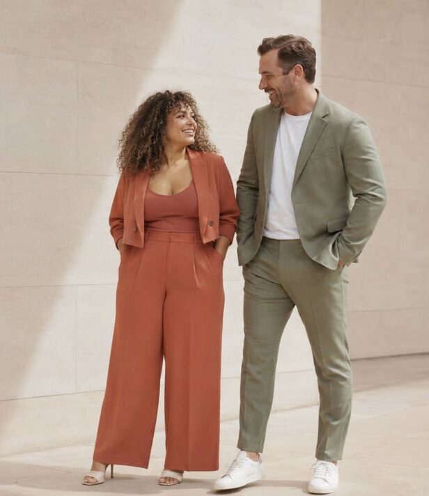 Women's rust jumpsuit and men's olive suit walking together outdoors
