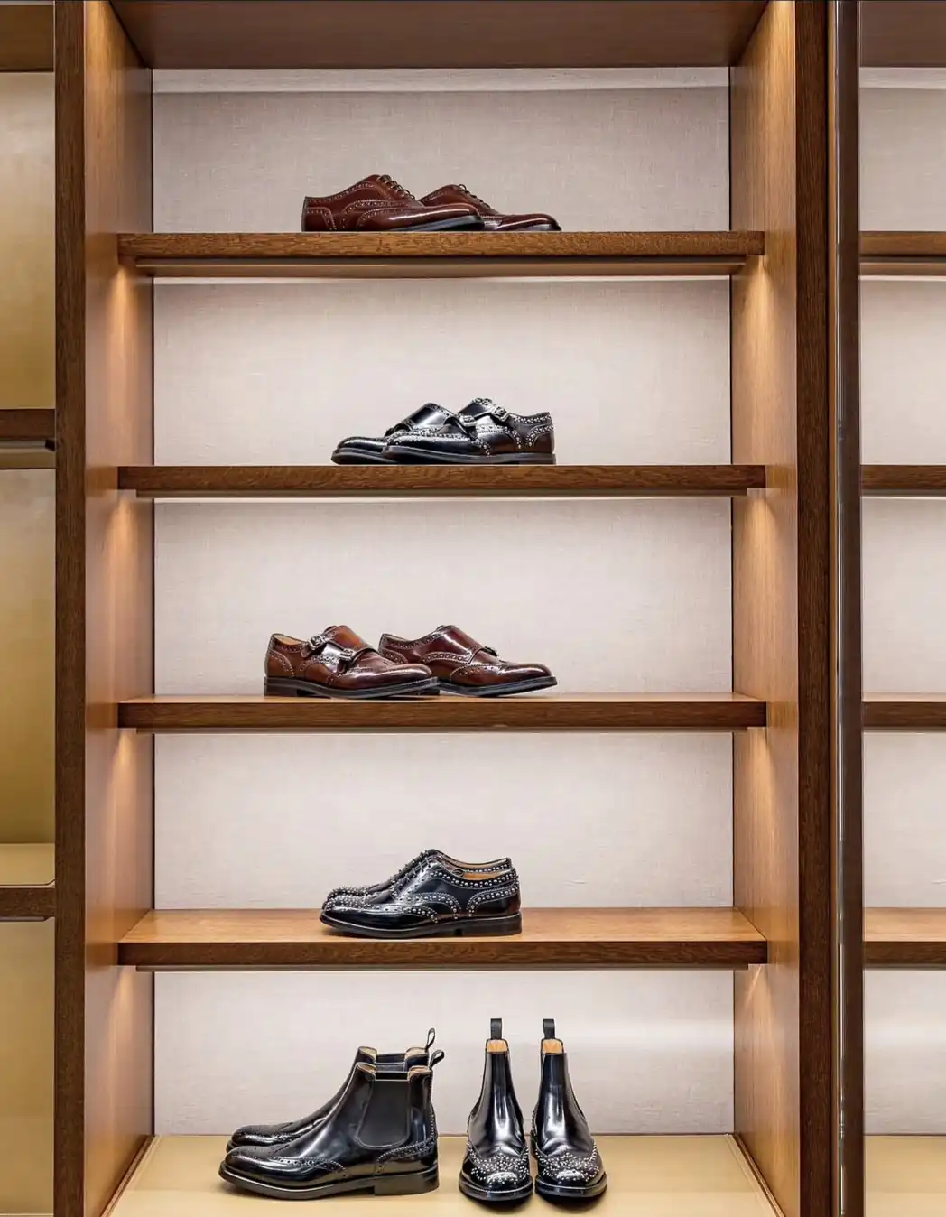Black and brown brogues and Chelsea boots on lit wooden display shelves