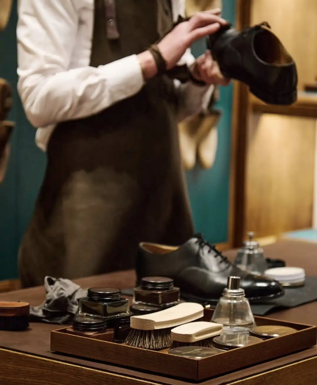 Black Oxford shoe on a polishing table with brushes, creams and a leather apron